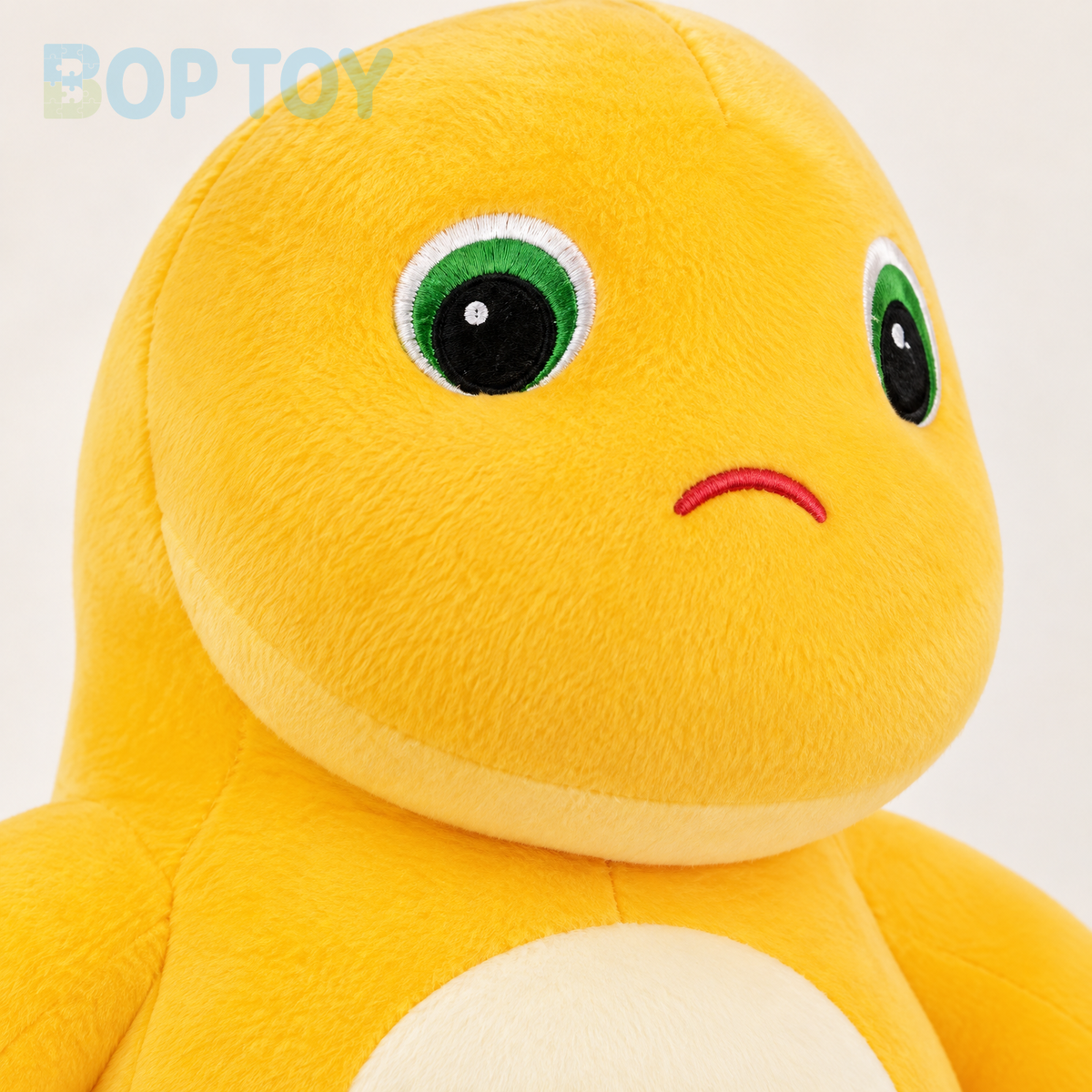 Close-up of yellow dinosaur plush embroidered green eyes and tiny frown